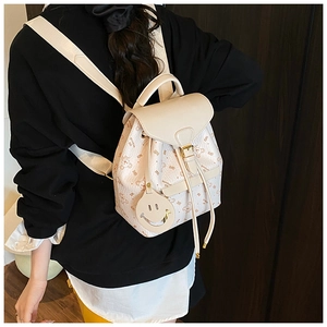 Detail of cream backpack with cartoon bear prints and smiley charm on a model