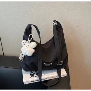 Close-up of a black textured nylon shoulder bag with a white plush doll charm accessory