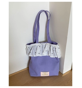 Detail of purple canvas tote bag featuring white floral lace trim and a pink woven label