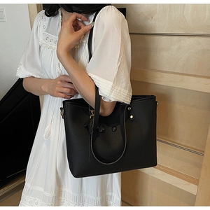 Detail of black pebbled leather tote bag with gold hardware and outer pocket on wood stairs