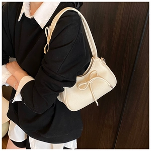 Close-up of cream bow-knot shoulder bag in lychee pattern leather worn by a model
