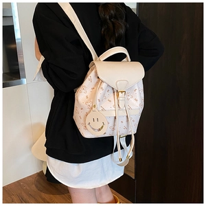 Detail of cream white backpack featuring cartoon bear print and smiley face pendant charm