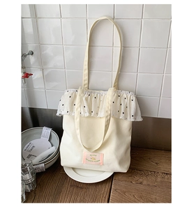 Close-up of white canvas tote bag with polka dot ruffle trim and pink label detail