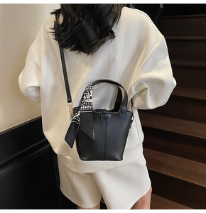 Detail of black leather bucket bag featuring a houndstooth scarf and gold hardware