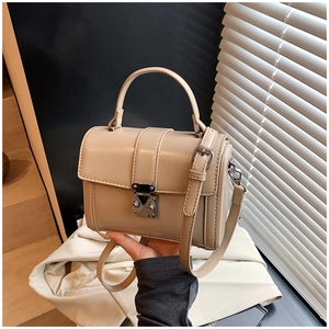 Detailed view of beige faux leather handbag with silver lock and adjustable strap