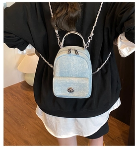 Mini light blue denim backpack with silver chain strap shown worn by a model in a room