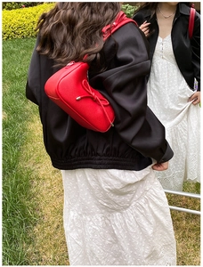 Detail of red pebbled leather shoulder bag with a long tassel bow in a casual outdoor setting