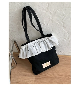 Detail of black canvas tote bag featuring white lace ruffle trim with floral pattern