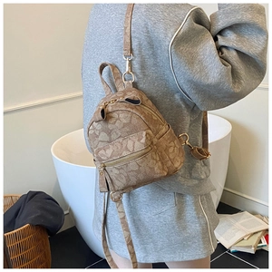 Rear view of a model wearing a mini khaki backpack with brown floral prints and gold zippers