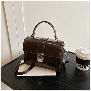 Detail view of glossy dark brown square handbag with silver metal buckle on black wood surface