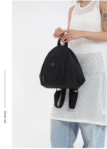 Detail of a black mini nylon backpack showing front zipper pocket and metal logo
