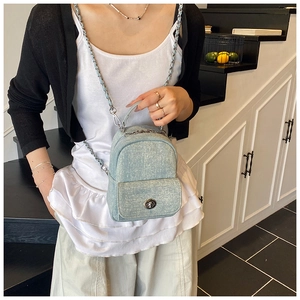 Detail of light blue denim mini bag with silver chain strap and metal turn-lock closure