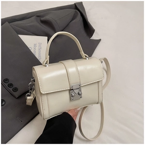 Detailed shot of cream faux leather handbag featuring silver buckle and round handle