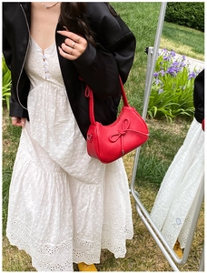 Detail of red lychee pattern leather shoulder bag with decorative bow in outdoor setting