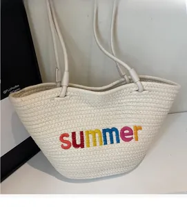 Close-up of woven straw tote bag featuring colorful summer embroidery and rope handles