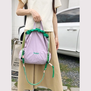 Detail of light purple nylon drawstring bag with green cords and colorful woven strap