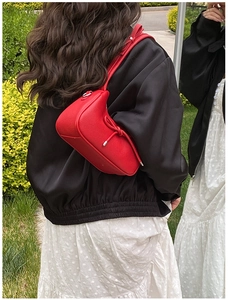 Outdoor shot of a red pebbled leather crescent bag with bow detail worn as a shoulder bag