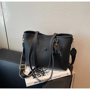 Close-up of black lychee leather tote bag with wide bicolored fabric strap and elephant charm