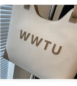 Detail of lychee pattern leather tote bag with WWTU stitched letters and brown trim