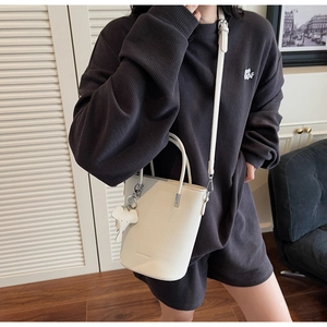 Detailed shot of white bucket bag with animal charm and adjustable leather strap