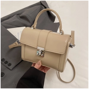 Detail of a beige structured handbag with silver twist lock on a grey suit jacket