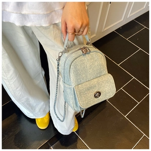 Macro shot of light blue denim backpack with silver zipper and chain shoulder strap