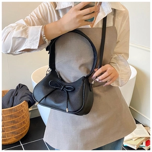 Detailed view of a black pebble leather half-moon bag with bow detail and wide shoulder strap