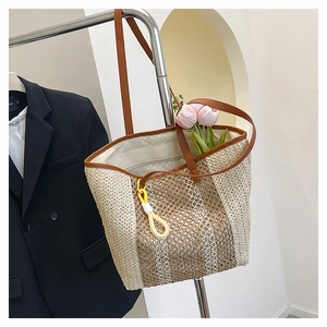Detail of two-tone woven straw beach bag featuring brown leather handles and decorative rope