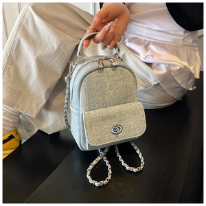 Detail of light blue denim mini backpack featuring silver turn-lock and chain straps
