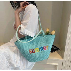 Close-up of light blue woven tote bag with colorful summer embroidery on white dress
