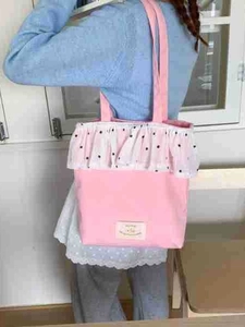 Pink canvas tote bag with polka dot ruffle trim shown as a casual shoulder bag for women
