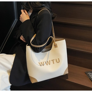 Detail of a large cream leather tote bag with brown trim shown in a commute style scene
