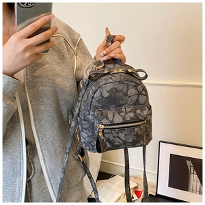 Close-up of mini backpack with leaf patterns and golden metal zipper held by model
