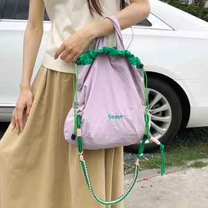 Detail of nylon crossbody bag featuring green drawstring and embroidered beaut text logo