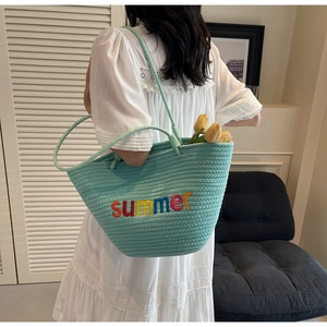 Detail of mint green woven tote bag featuring colorful summer embroidery and slim straps