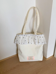 Minimalist off-white canvas tote bag with floral ruffle trim and wide shoulder straps