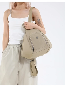 Side view of beige nylon backpack showing adjustable straps and round metal logo detail