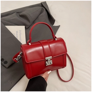 Detail showing red glossy leather texture and silver buckle on a minimalist square bag