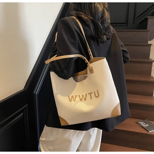 Detail view of large cream and brown leather tote bag with WWTU lettering carried on shoulder