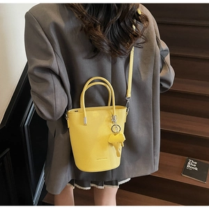 Yellow bucket bag with lychee pattern and elephant charm worn over a gray blazer