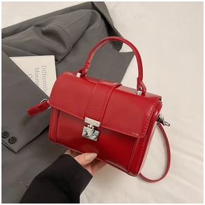 Detail of red glossy structured handbag featuring silver metal square lock and top handle