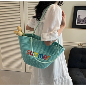 Detail of mint green woven tote bag featuring colorful summer embroidery and slim straps