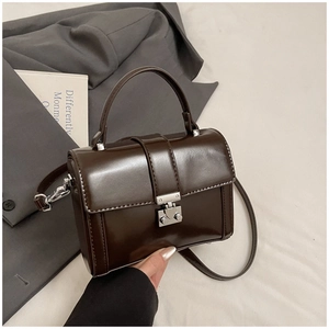Detail of dark brown polished leather crossbody bag with elegant silver metal lock