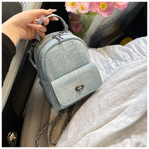 Detail of light blue denim mini backpack with silver chain strap on a car seat