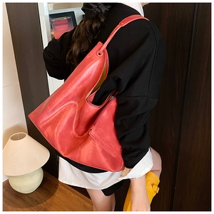 Detail of red leather hobo tote bag worn by a model in a cozy indoor setting