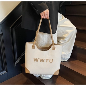 Detail of a beige tote bag with brown leather trim and WWTU lettering on stairs