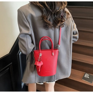 Detail of red litchi leather bucket bag with top handles and cute elephant charm