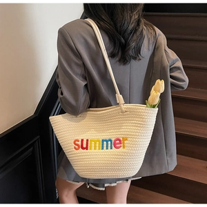 Close-up of cream woven tote bag with colorful summer embroidery on a model's shoulder