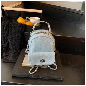 Detail of a light blue denim mini backpack with silver metal chains and rotary lock