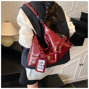 Close-up of deep red glossy leather tote bag with woven handle and brand tag detail
